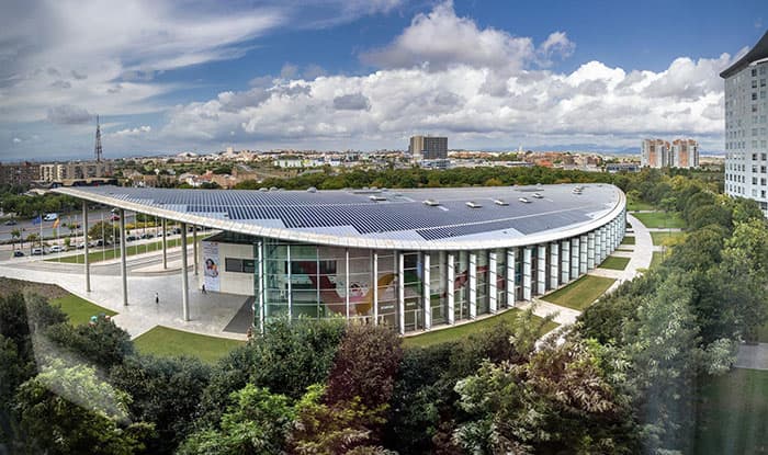 Ein modernes Gebäude mit geschwungenem Glasdesign und Solardach in einer grünen Umgebung bei bewölktem Himmel