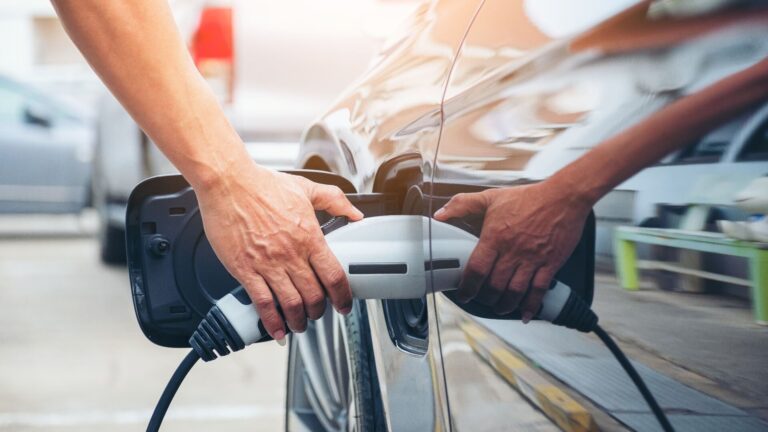 Eine Person mit neutralem Gesicht lädt ein silberfarbenes Elektroauto auf