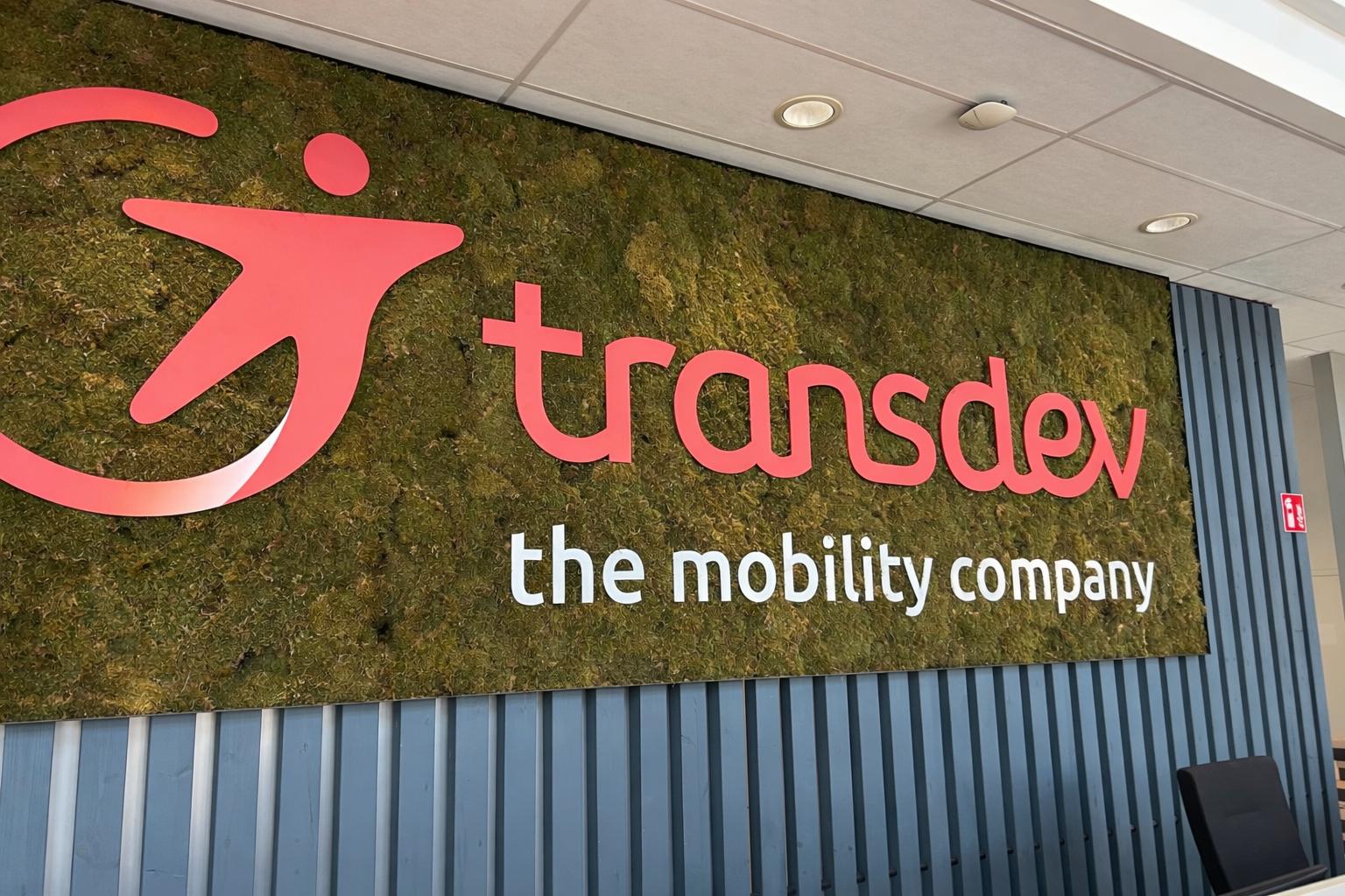 Ein modernes Wandlogo von Transdev auf Moos mit roten Buchstaben und grauer Wand